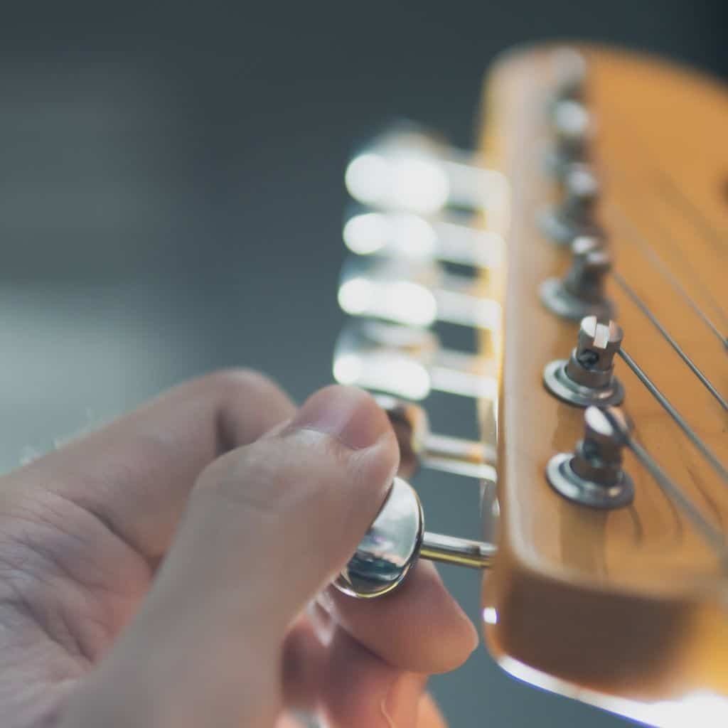 A Guitarist Hands Tuning The Guitar Using The Tuning Pegs