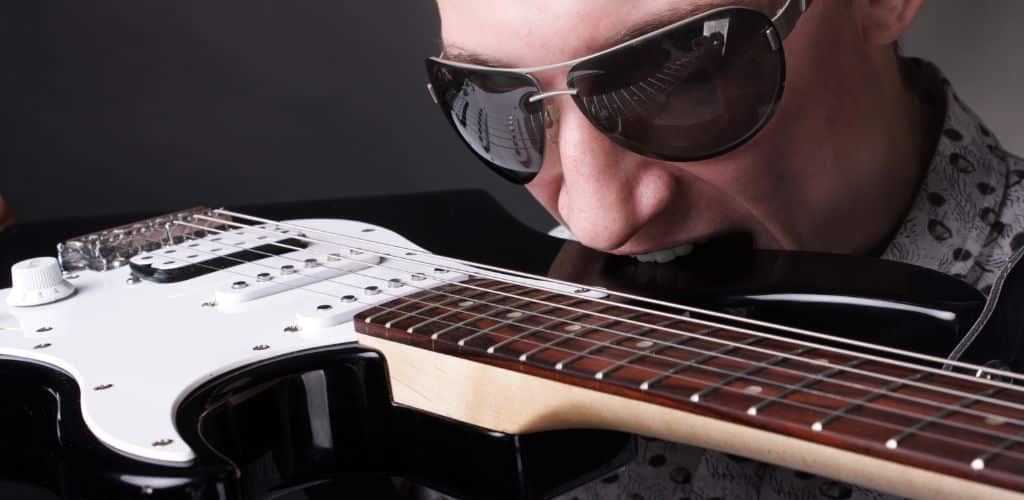 10 Crazy Things Guitarists Have Used To Play Solos—You Won'T Believe What’s On This List! An Electric Guitarist Biting A Black Electric Guitar