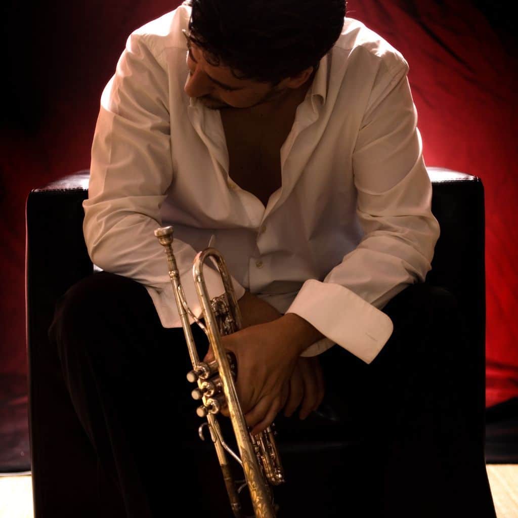 From Wall Street To Jazz Stages: The Journey Of Jonathan Dely A Jazz Trumpet Sitting On A Single Couch While Holding His Trumpet