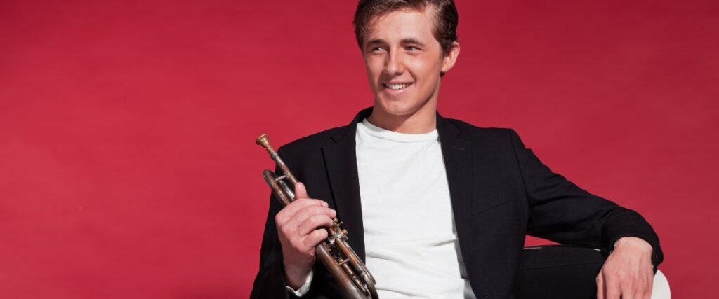From Wall Street To Jazz Stages: The Journey Of Jonathan Dely A Smiling Jazz Trumpet Player Holding His Trumpet While Sitting On A White Chair