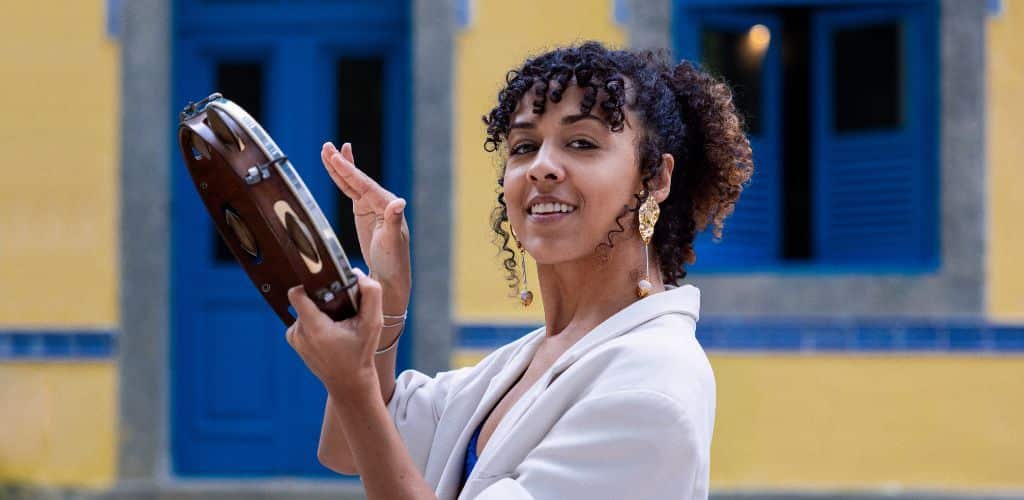 Smallest Instrument In The World A Woman Playing A Tambourine While Smiling At The Camera