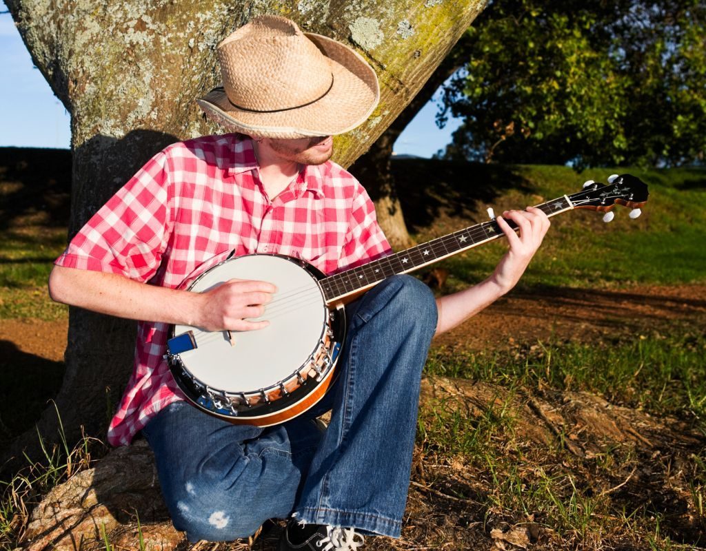 A Banjo Player Wearing A Hat Playing The Banjo Under A Tree A Banjo Player Wearing A Hat Playing The Banjo Under A Tree