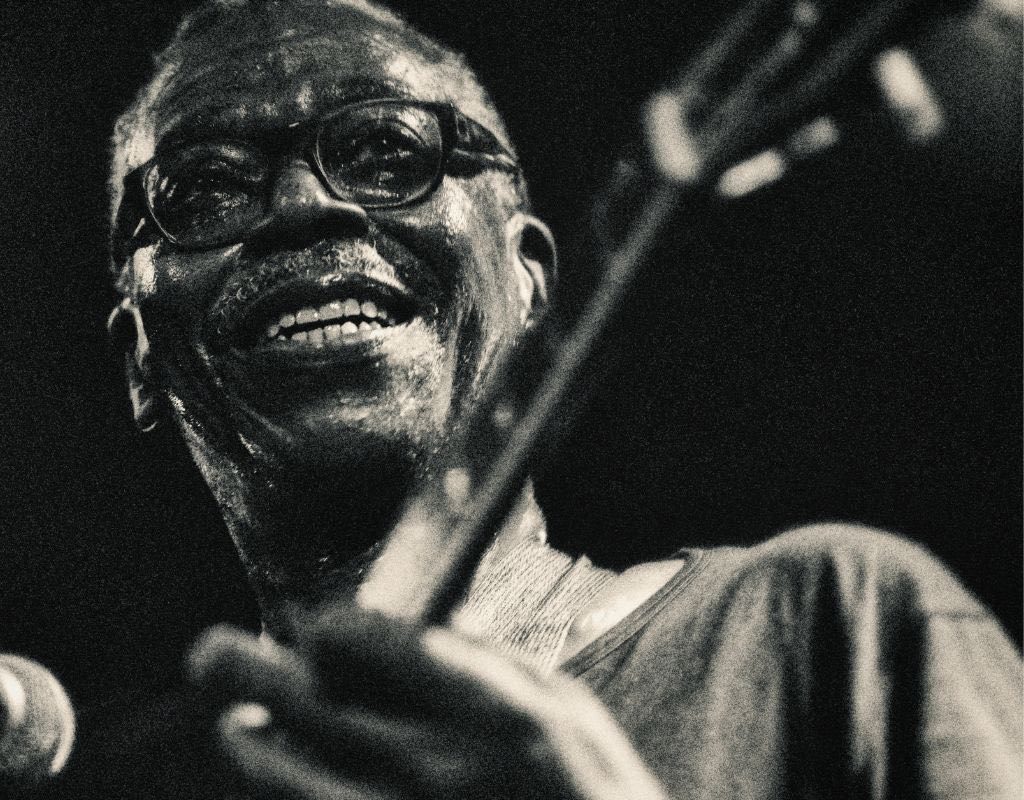 A Black And White Photo Of A Smiling Guitarist Performing On Stage A Black And White Photo Of A Smiling Guitarist Performing On Stage