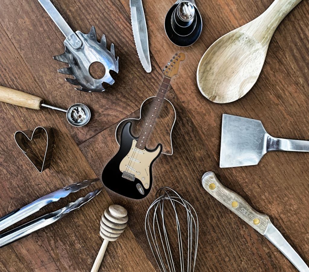 A Black Electric Guitar With Kitchen Utensil On The Background A Black Electric Guitar With Kitchen Utensil On The Background