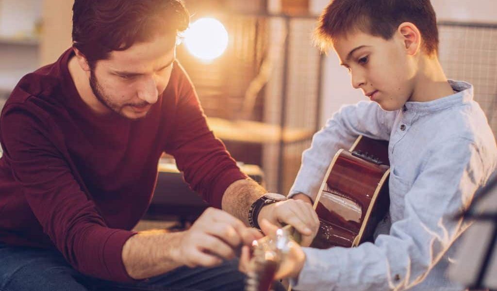 A Guitar Teacher Guiding The Finger Position Of His Student