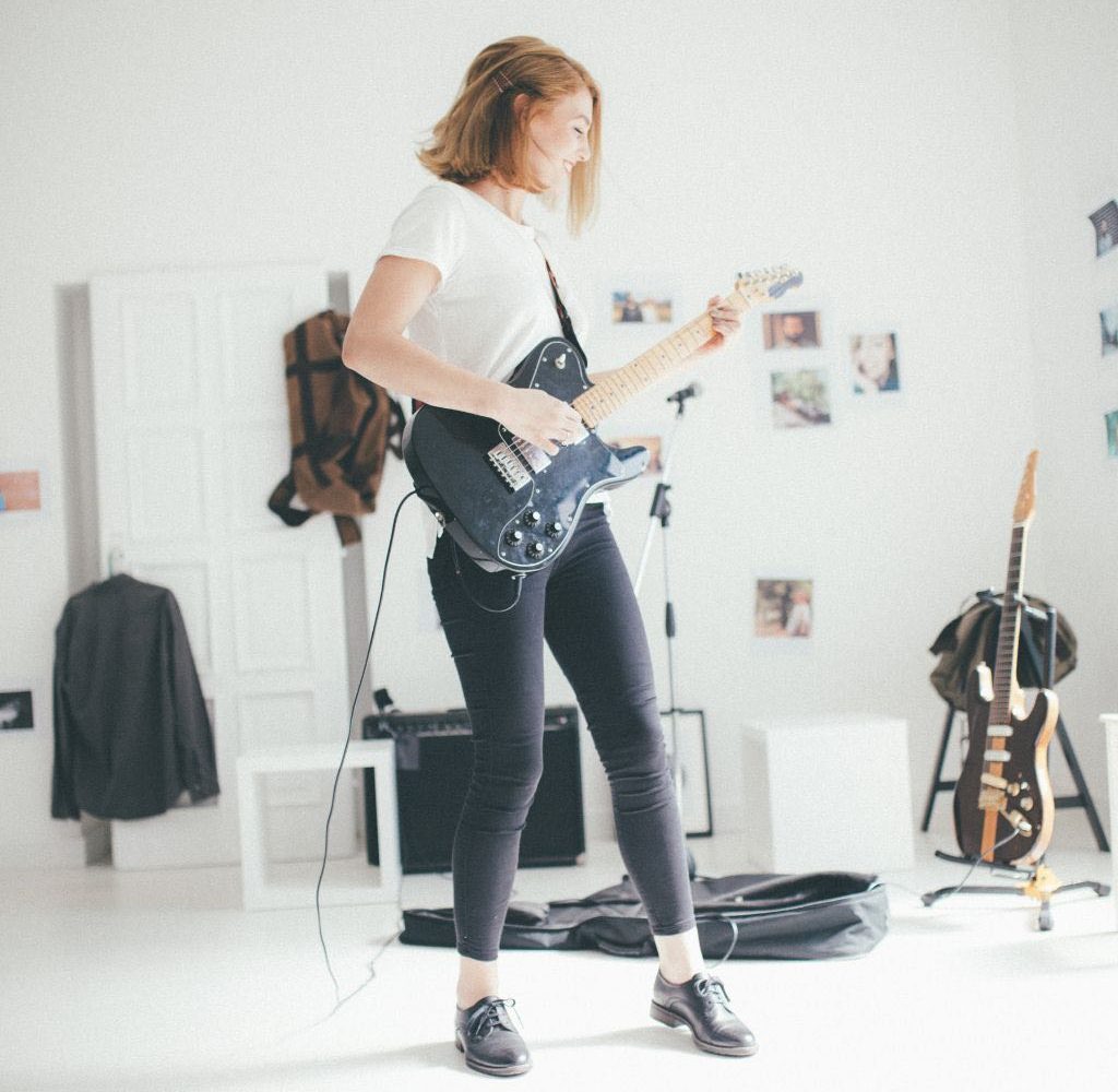 A Woman Playing A Black Electric Guitar Inside A Bright Room A Woman Playing A Black Electric Guitar Inside A Bright Room