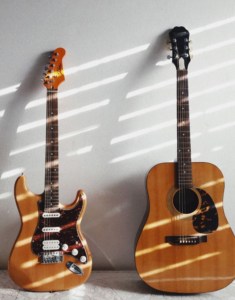 An Electric And Acoustic Guitar Leaning On A White Wall An Electric And Acoustic Guitar Leaning On A White Wall